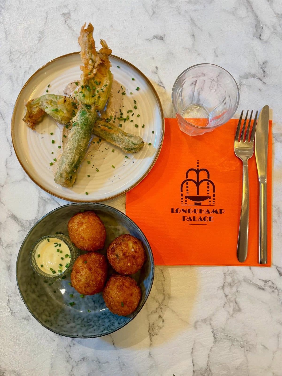 Fleurs de courgette en beignet et croquettes, dressées sur la serviette au logo de la maison.