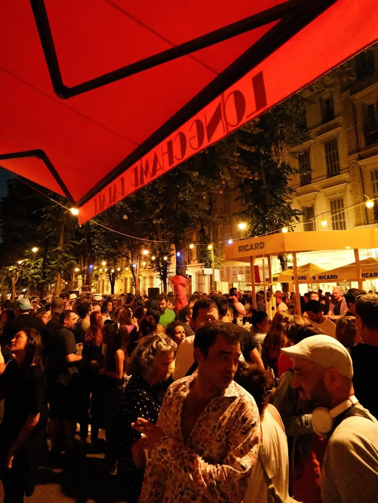Le store rouge du Longchamp Palace au-dessus de la foule, un soir de fête sur le boulevard.
