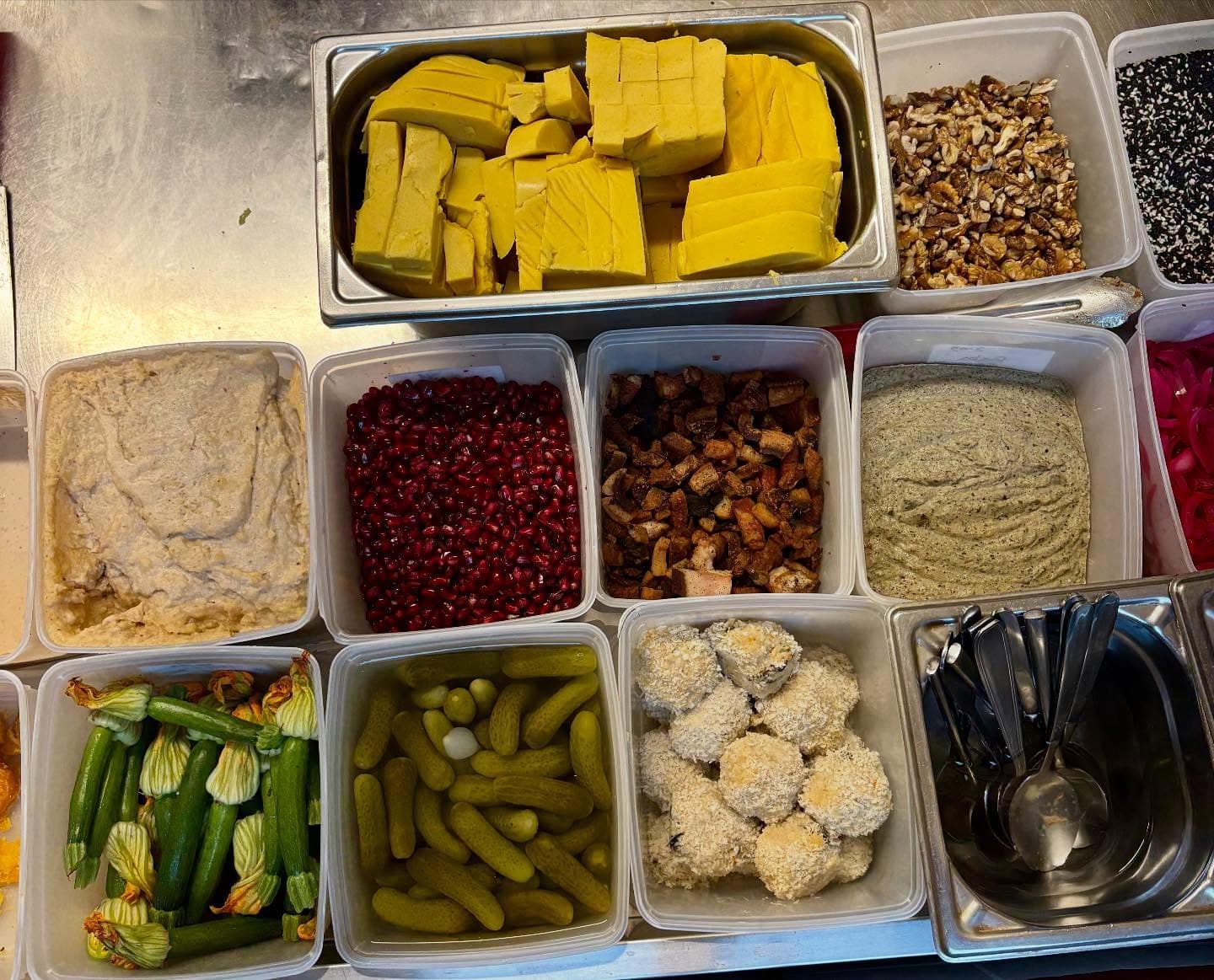 La mise en place vue de dessus : bacs de légumes, de graines, de purées et de cornichons alignés sur le plan de travail.